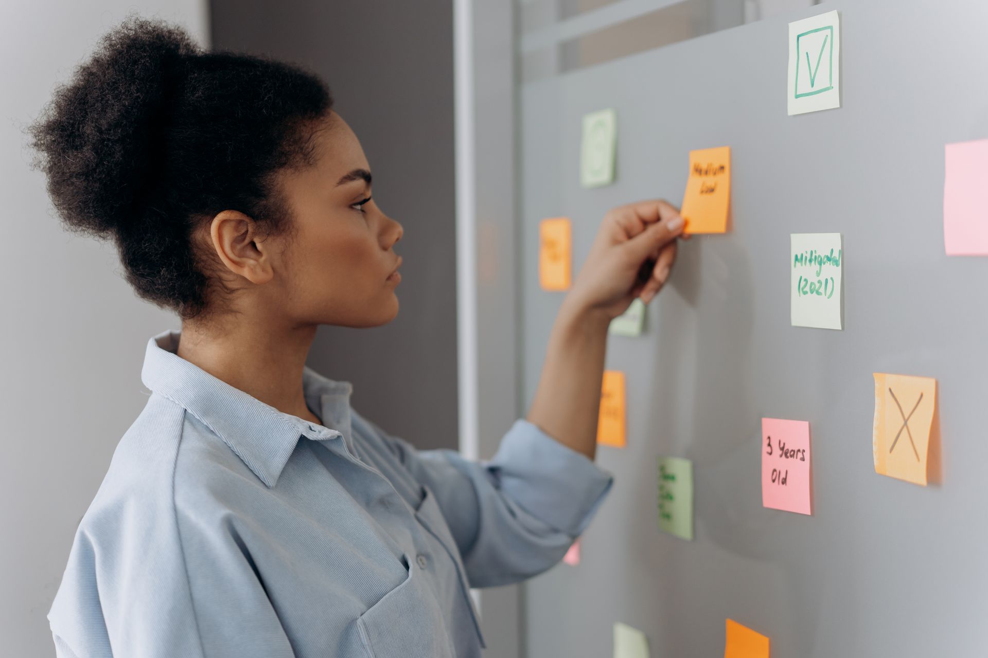 Mujer ordenando notas adhesivas de colores en una pizarra para priorizar tareas